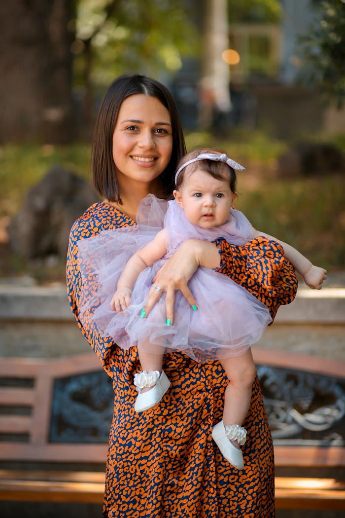 A joyful mother holding her baby daughter outdoors in a park setting.