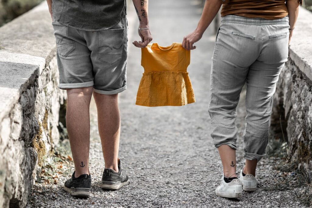 A couple standing outdoors holding a yellow baby dress symbolizing a future addition to their family.